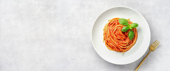 Top view of plate eith pasta in tomato sauce and basil on white background