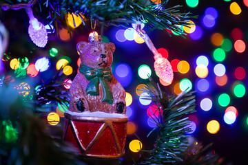 Close-up of a shiny Christmas decoration in the form of a bear on a drum hanging on a Christmas tree in the background many garlands in different colors glow. New Year and Christmas concept.