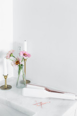 Modern hair straightener on white marble countertop, brass decor with candles and flowers, bobby pins, girly bathroom, copy space