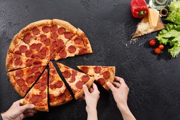 Pepperoni pizza on a black background texture. Still life with hands and ingredients. Copy space.