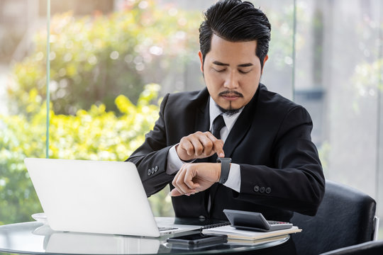 business man checking time on smart watch while using laptop
