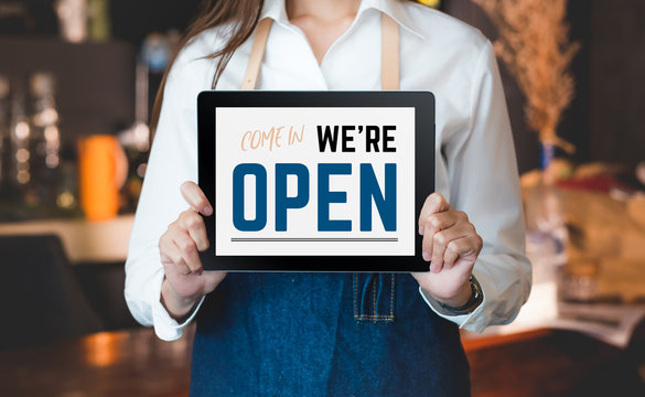 Woman Barista Wear Jean Apron Holding Come In We Are Open Sign On Tablet To Customer At Bar Counter With Smile Emotion,Cafe Restaurant Service Concept,Owner Of Start Up Small Business.