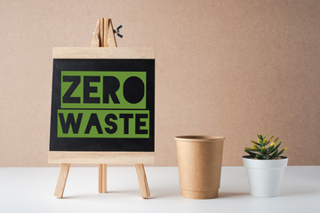 zero waste word on blackboard with peper cup and green plant on white table and brown...