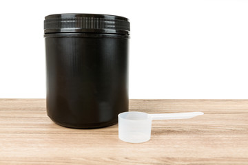 Black supplement tub with scoop on a wood patterned background