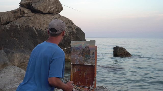 Plein Air painting. A professional artist man painting of the sea and cliffs, landscape, seascape, summer sunset