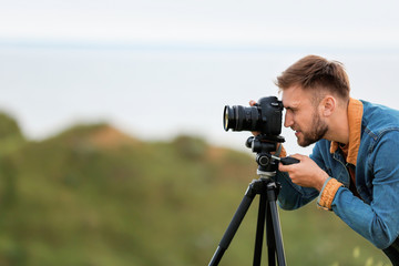 Male photographer taking picture of beautiful landscape with professional camera on green hill. Space for text