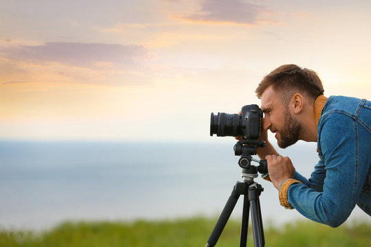 Male photographer taking picture of beautiful landscape with professional camera outdoors. Space for text