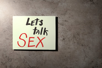 Note with phrase "LET'S TALK SEX" on stone background, top view