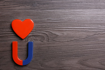 Red and blue horseshoe magnet with decorative heart on dark grey wooden background, flat lay. Space...