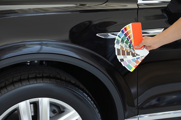 Young woman holding palette with color samples near black car, closeup