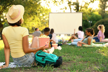 Young woman with popcorn watching movie in open air cinema. Space for text
