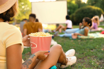 Young woman with popcorn watching movie in open air cinema, closeup. Space for text - obrazy, fototapety, plakaty