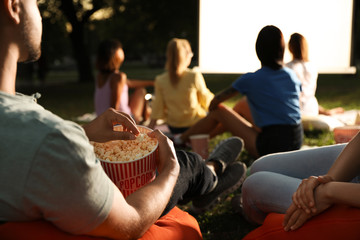 Young people with popcorn watching movie in open air cinema, closeup. Space for text - obrazy, fototapety, plakaty
