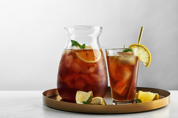 Jug and glass of delicious iced tea on table against light background