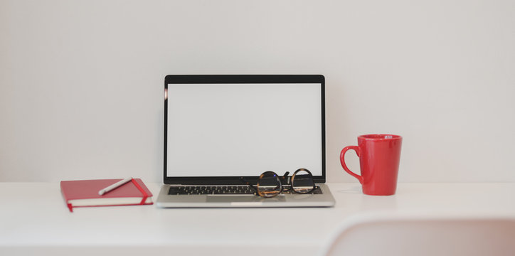 Close-up view of modern office with laptop computer, red notebook and red coffee cup