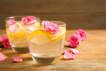 Tasty refreshing lemon drink with roses on wooden table