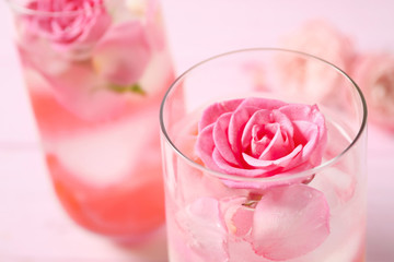 Delicious refreshing drink with lemon and roses on pink wooden table, closeup