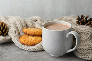 Delicious hot cocoa drink in cup, cookies and knitted blanket on grey surface
