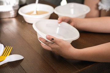 Poor little child holding empty plate over wooden table in charity centre, closeup