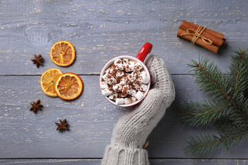 Person holding cup of tasty cocoa with marshmallows on grey wooden table, top view