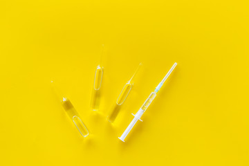 Flu vaccination. Ampoule and syringe on yellow background top view space for text