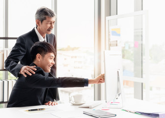 The young businessman smiling and checking the point to the screen. He is discussing with his boss on the desk in his office room.