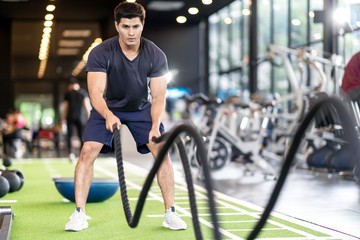 Sporty asian man exercising with battle ropes at the gym on green floor. Strong male determine with...