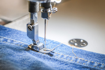White industrial sewing machine sew seam of blue jeans close-up.