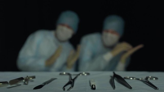 Surgeons dance before or after operation or procedure in hospital. Funny and comic situation. Focus on surgical instruments lying in foreground. Successful hours-long surgery completed
