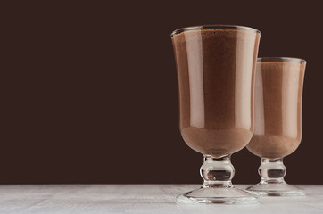 Christmas beverage - hot chocolate in transparent goblet on elegant dark brown interior, copy space.
