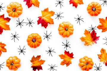 Fototapeta premium Nice halloween background. Small spiders among leaves and pumpkins on white top view pattern