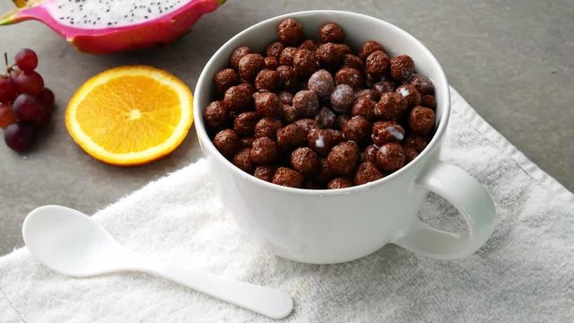 Pouring milk in a cup of chocolate cereal balls on table. Healthy breakfast concept.