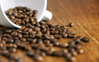 Coffee bean pouring out of a white mug on wooden table