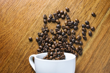Top view image of coffee bean pouring out of a white mug on wooden table
