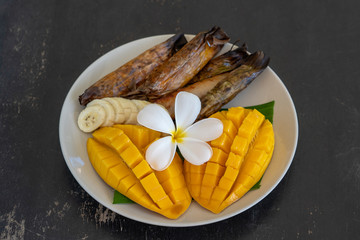 Thai style dessert, yellow mango with banana sticky rice in palm leaves. Yellow mango and sticky rice is popular traditional food of Thailand. Closeup
