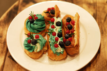 eclairs decorated with fresh berries on a white plate, handmade, culinary theme, close up