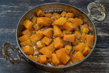 Baked yellow pumpkin with honey, anise, olive oil and spices on a plate on the wooden table. Vegetarian food. Closeup