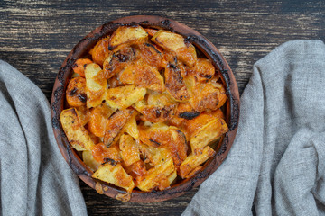 Baked potato and carrot with cheese on the wooden table, close up. Ceramic bowl with potato and carrot slices background