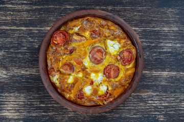 Ceramic bowl with vegetable frittata, simple vegetarian food. Frittata with tomato, pepper, onion and feta cheese on wooden table, close up. Italian egg omelette