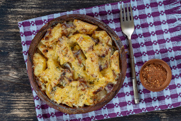 Baked potato, onion and garlic with cheese on the wooden table, close up. Ceramic bowl with potato onion and garlic slices background