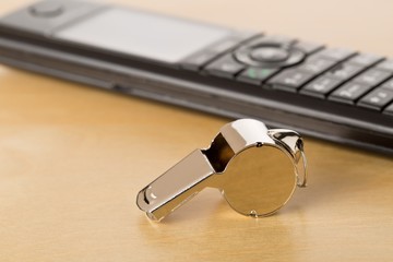 Chrome whistle with telephone on wooden office desk - whistleblower concept