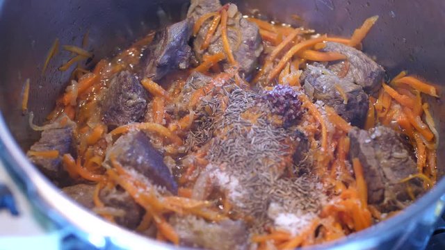 Adding spices to meat crots and carrots when cooking Plov traditional dish from Uzbekistan