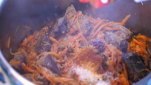 Adding spices to meat crots and carrots when cooking Plov traditional dish from Uzbekistan