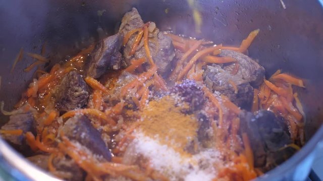 Adding spices to meat crots and carrots when cooking Plov traditional dish from Uzbekistan