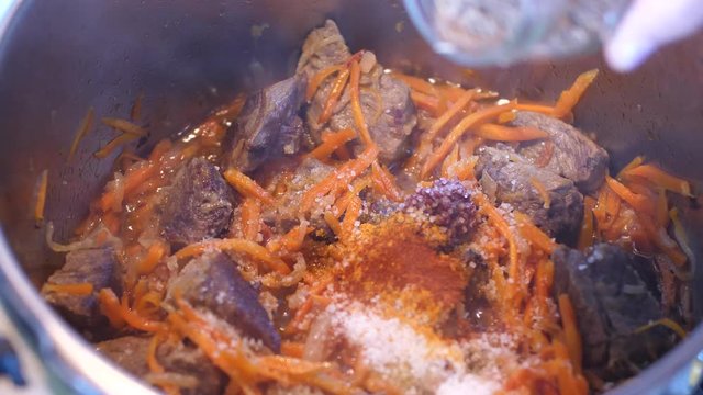 Adding spices to meat crots and carrots when cooking Plov traditional dish from Uzbekistan