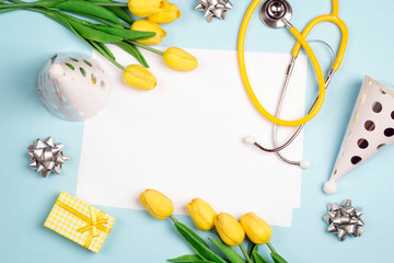 Doctor's or nurse day greeting card with stethoscope, yellow tulips and festive caps on blue background.