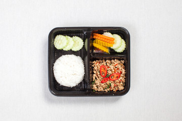 Basil fried rice with minced chicken, put in a black plastic box, put on a white tablecloth, food box, Spicy fried chicken with basil leaves, Thai food.