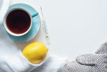 Cup of hot tea, thermometer, lemon and scarf on a white table background.