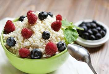 Cottage cheese in green bowl with raspberries and blueberries on wooden background. Healthy Breakfast.