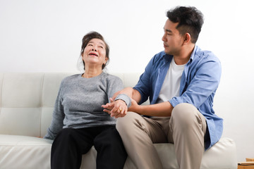 Asian senior woman mother and young man son in blue shirt massage his mother in living room